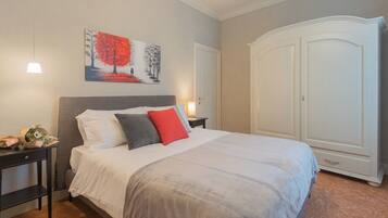 A bedroom with a large bed, a nightstand with a lamp, a painting on the wall, and a wardrobe.