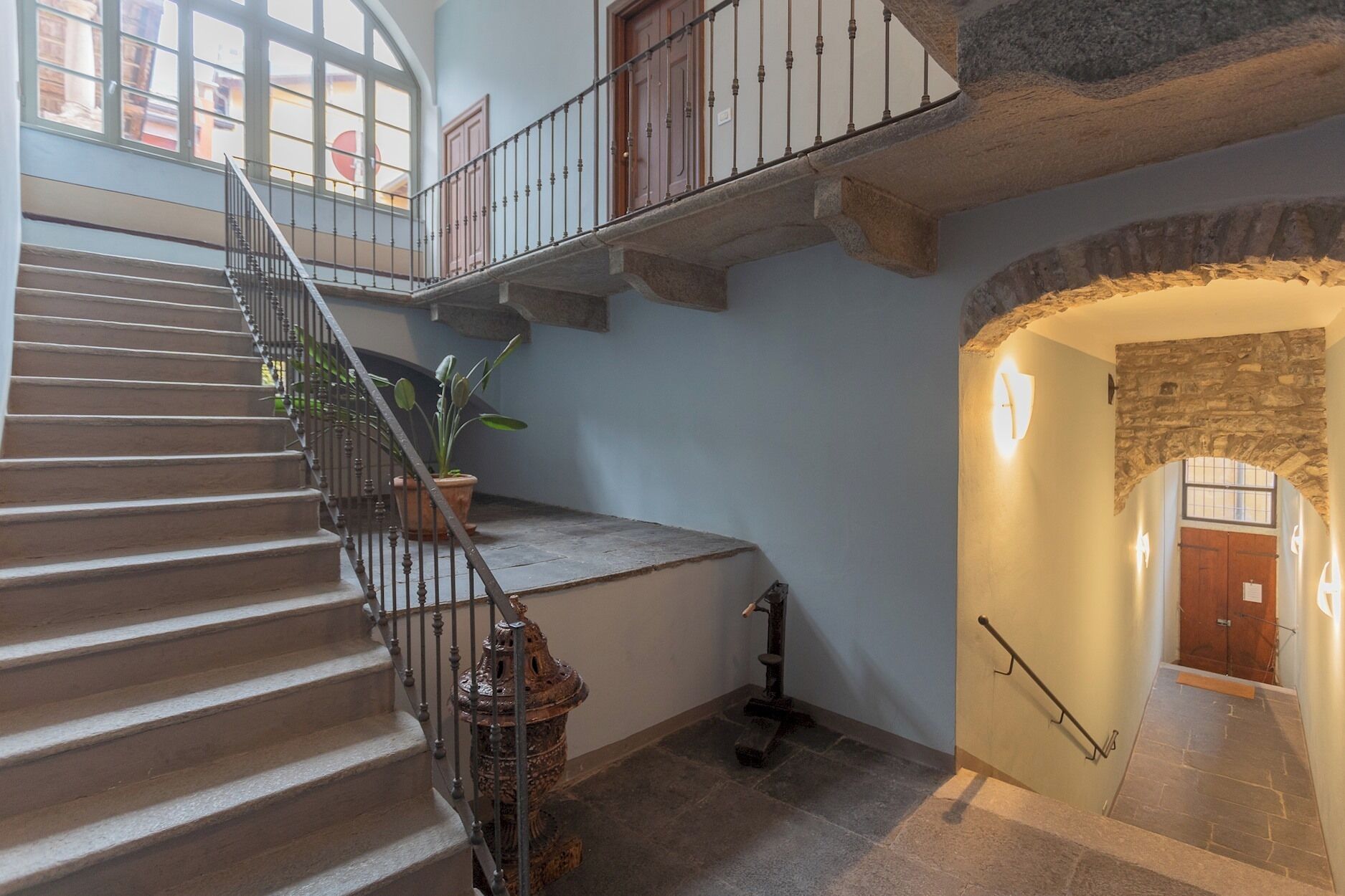 A grand staircase with a wrought iron railing, a potted plant, and a stone wall.