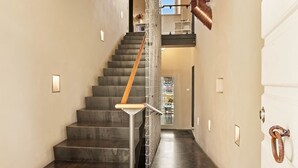 Un escalier moderne avec une main courante en bois, des rampes en métal et, au fond, une vue sur un coin repas.