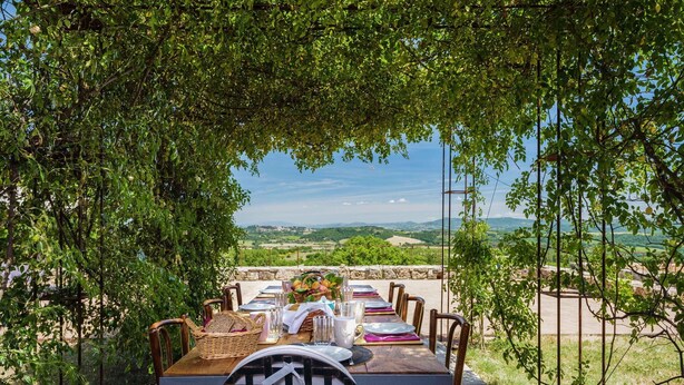 Un espace de restauration en plein air avec une table dressée pour quatre personnes, entouré de verdure et offrant une vue sur un paysage pittoresque.