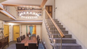 Un coin repas avec une table et des chaises en bois, un lustre et un escalier doté d’une rampe en bois.