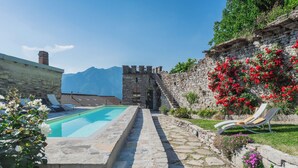 Une piscine en pierre, des chaises longues et un mur de pierre orné de fleurs rouges.