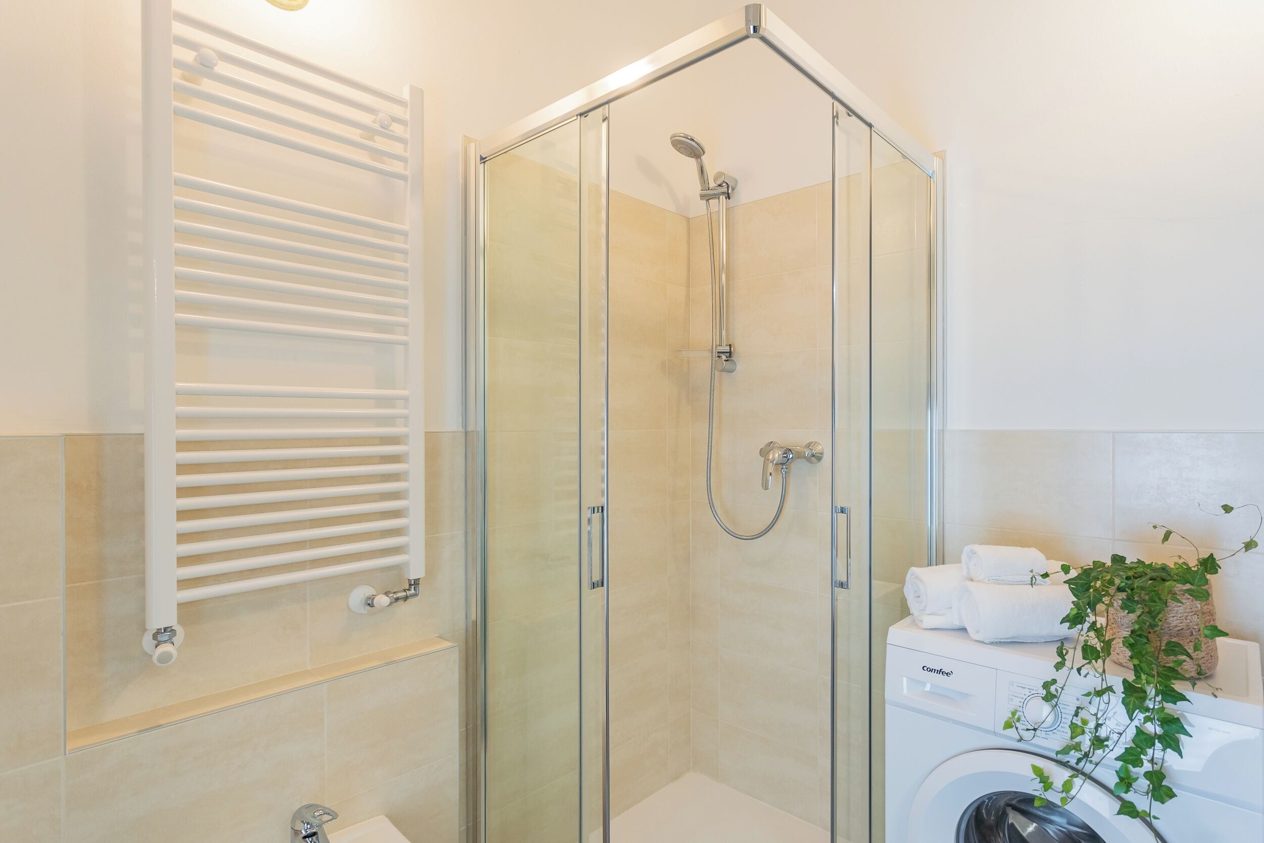 Une douche en verre avec un pommeau de douche amovible, un porte-serviettes blanc et un lave-linge avec des serviettes.