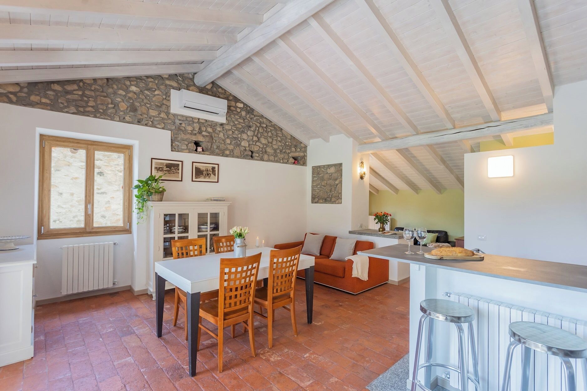 A cozy kitchen with a stone wall, wooden ceiling beams, and a dining area with a table and chairs.