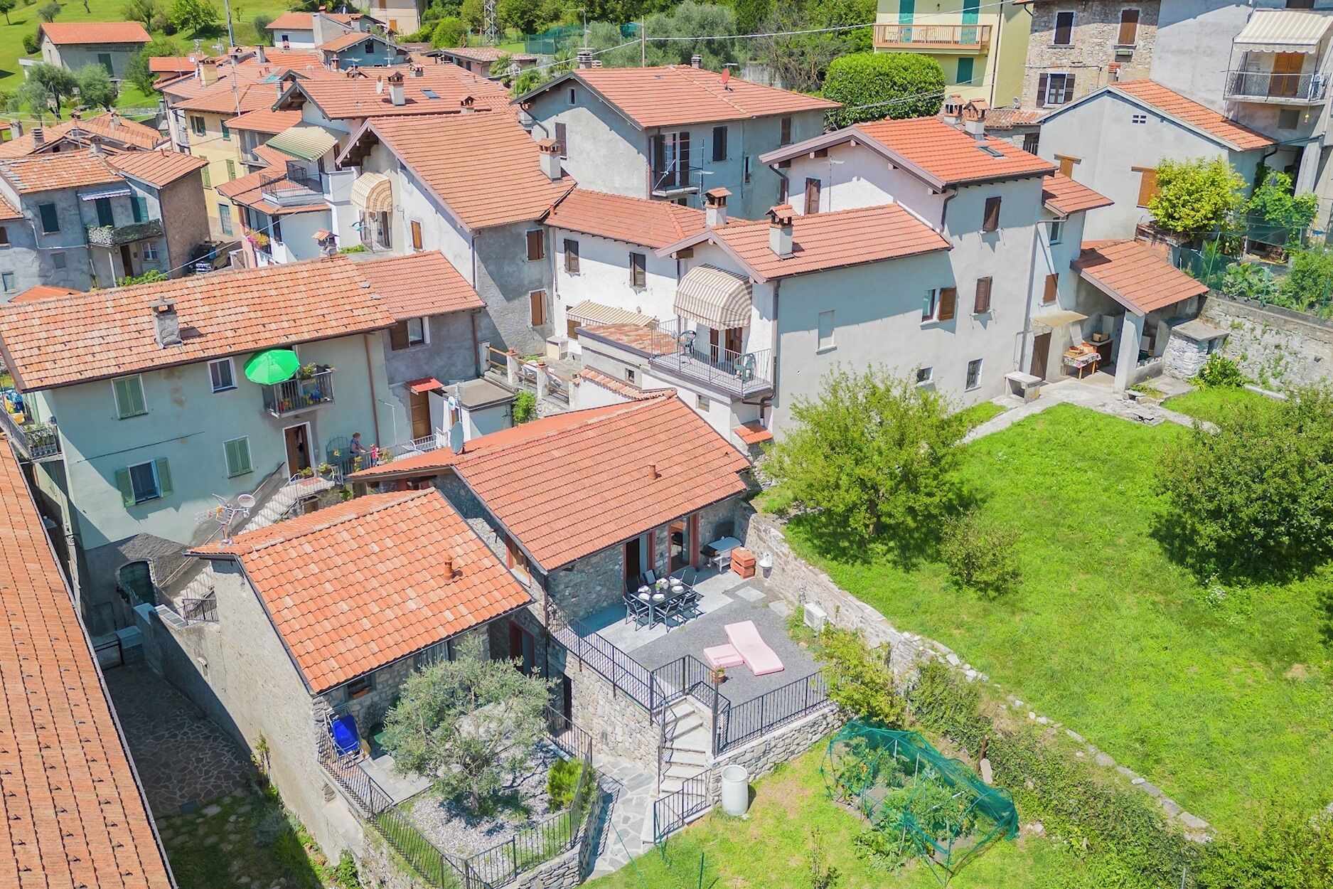 A residential area with terracotta-tiled roofs, stone buildings, and a green lawn.