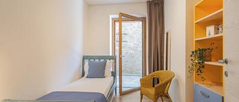 Une chambre à coucher avec un lit, une chaise, une armoire et une vue sur l’extérieur, visible à travers une porte.