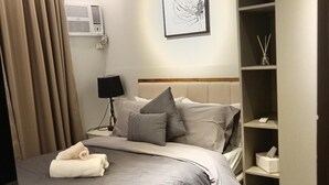 A modern hotel room with a large bed, a bedside table with a lamp, a wall-mounted air conditioner, and a built-in wardrobe. - Sweet Escape 7P at One Regis (Bacolod)
