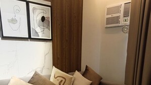 A modern living room with a grey sectional sofa, a round coffee table, and a vase with flowers. There are framed artworks on the wall and a window with curtains. - Sweet Escape 7P at One Regis (Bacolod)