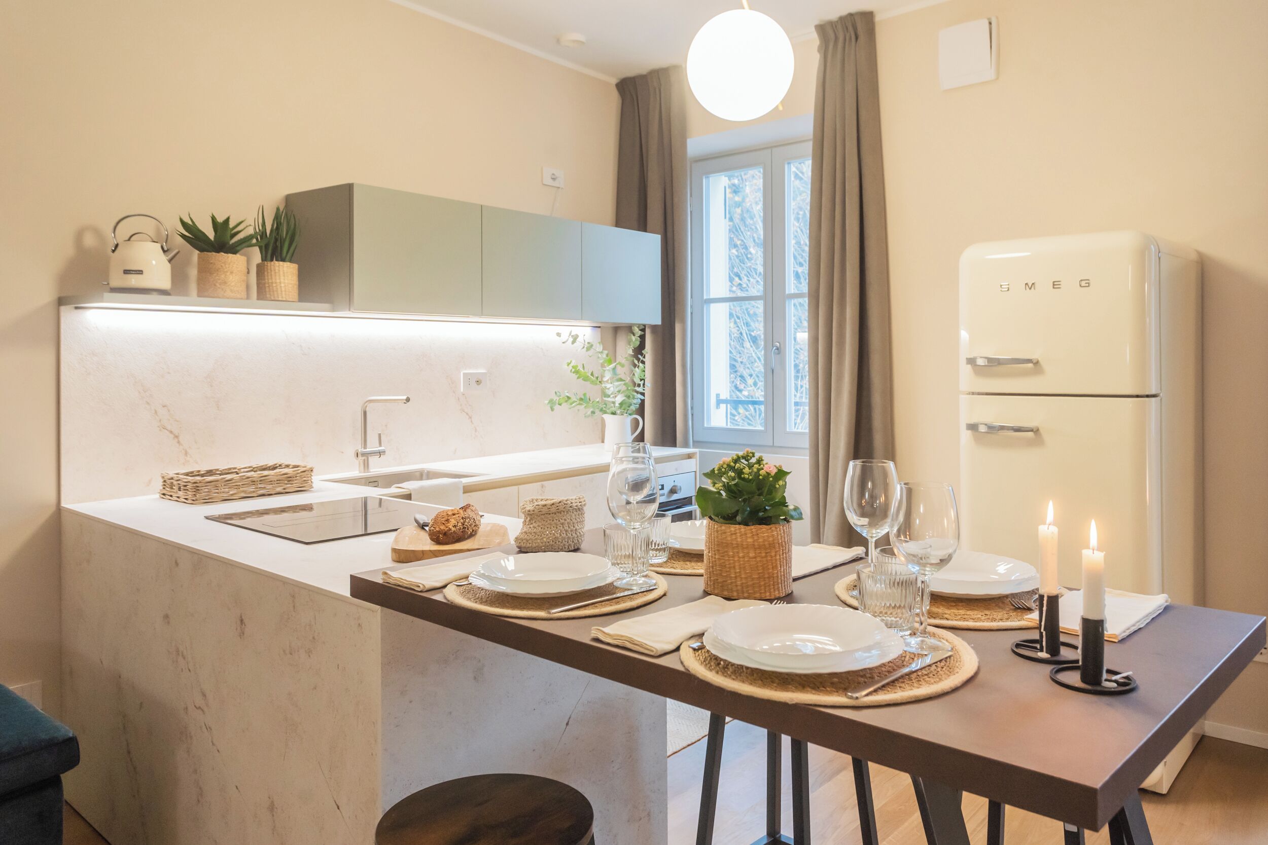 A modern kitchen with a marble countertop, a built-in oven, and a dining area set with plates, glasses, and candles.
