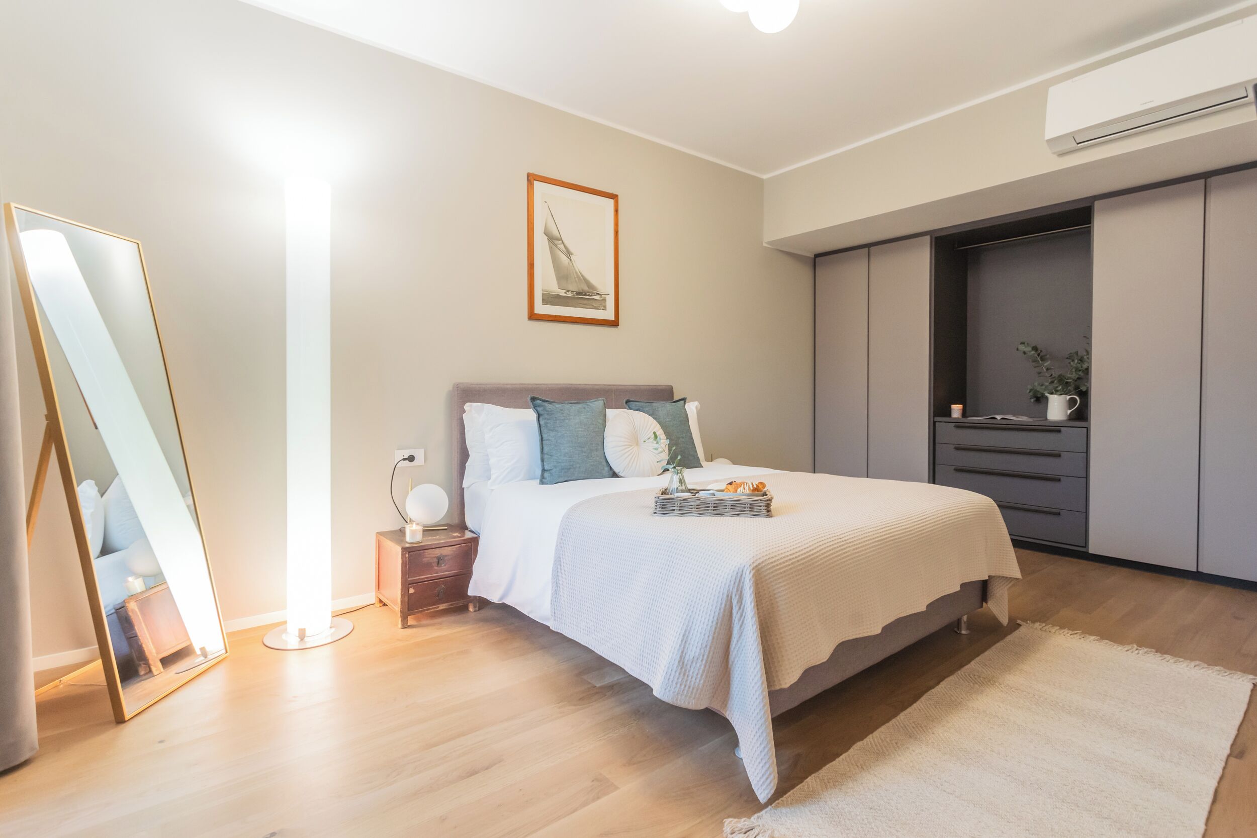 A bedroom with a bed, bedside table, mirror, wall-mounted artwork, and a wardrobe.