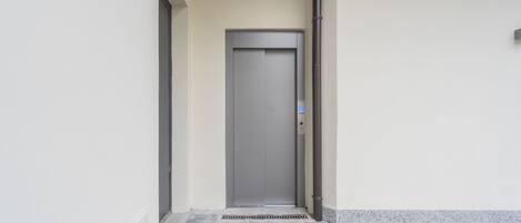 Entrada de un edificio moderno con una puerta cerrada, una pequeña rejilla de ventilación y suelo de baldosas.