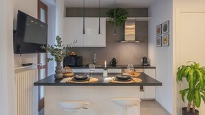 A modern kitchen with a central island, pendant lights, and a television on the wall. - We Lake Como by Rent all Como (Argegno)