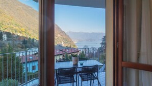 A balcony with a table and chairs, overlooking a mountainous landscape and a body of water. - We Lake Como by Rent all Como (Argegno)