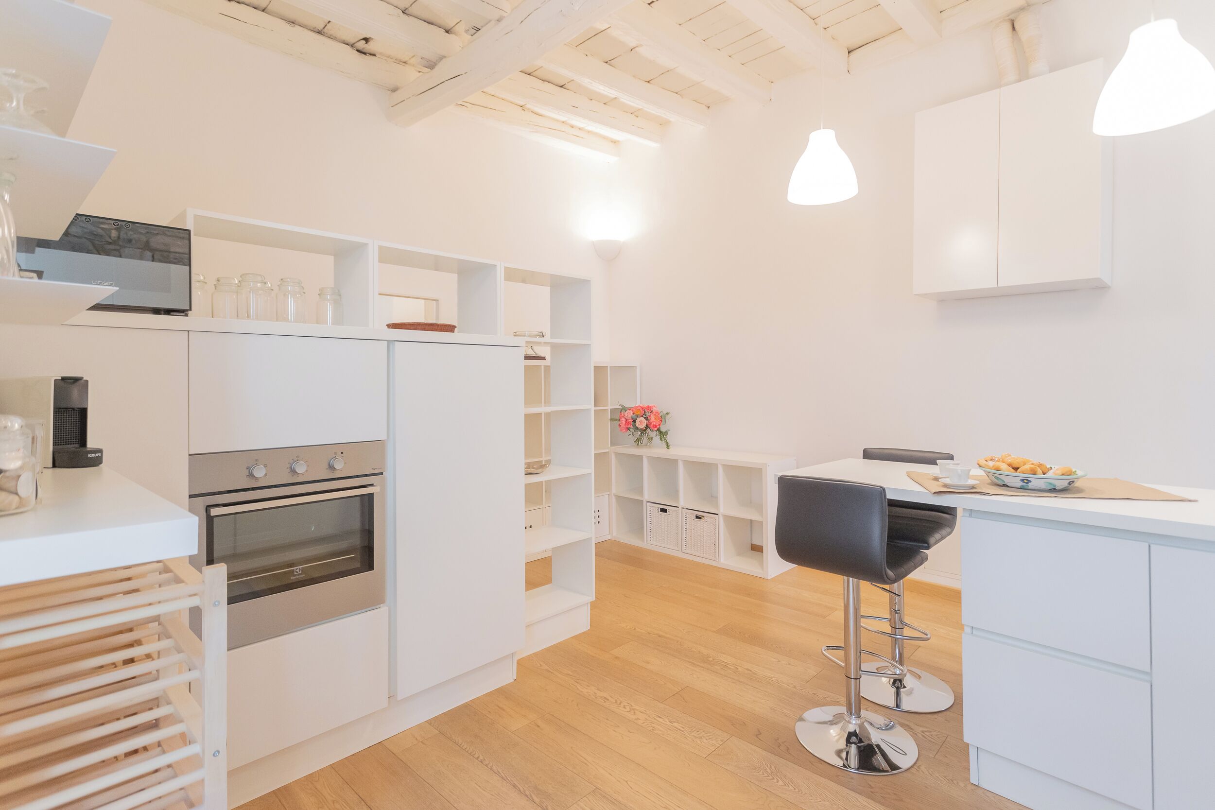 Une cuisine moderne avec des meubles blancs, un four encastré et un coin bar avec des tabourets.