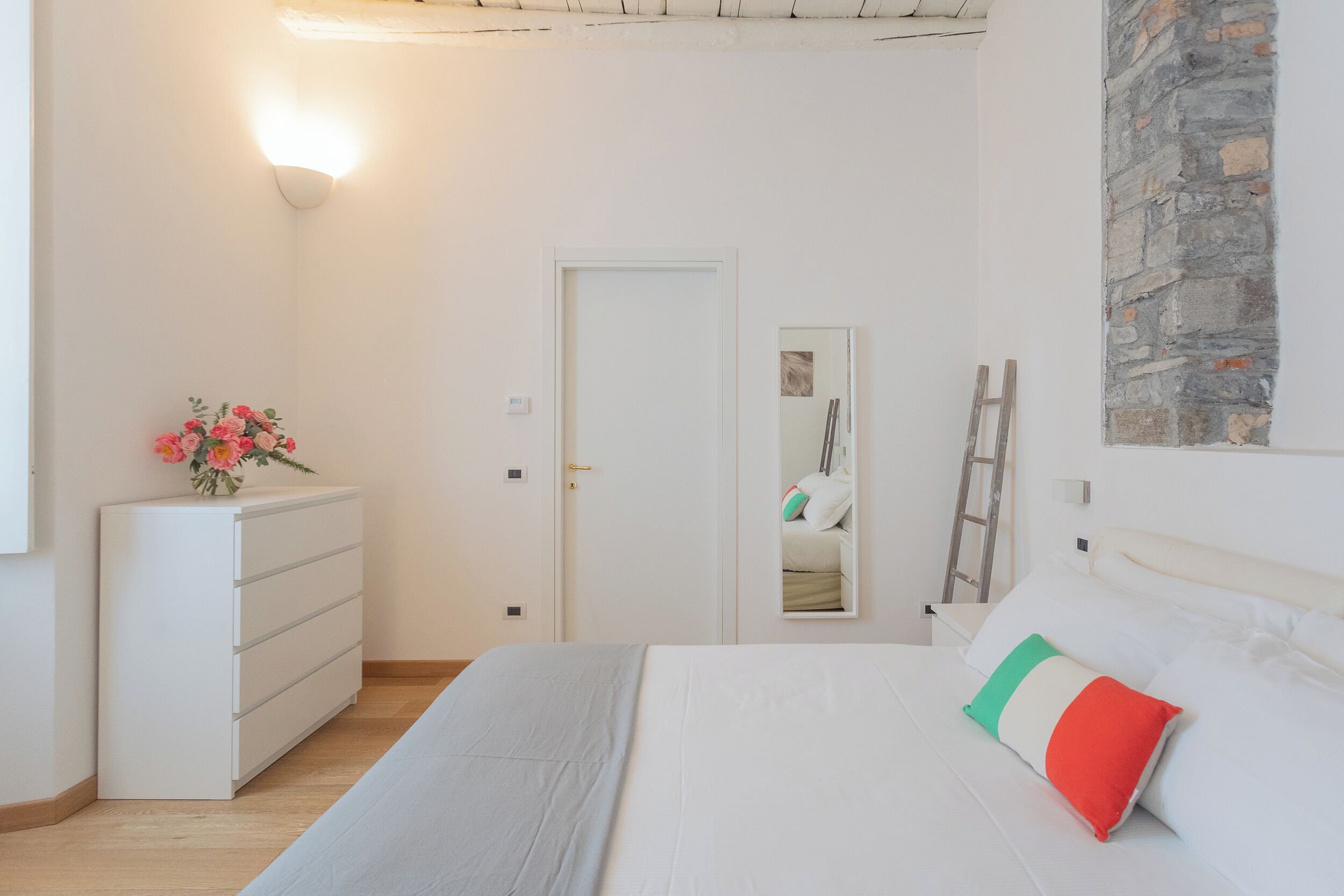 A bedroom with a bed, a dresser, a mirror, and a wall-mounted light fixture.