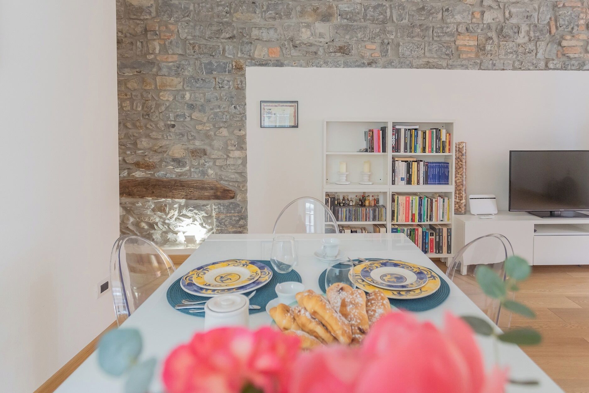 A dining area with a stone wall, a bookshelf, and a TV.