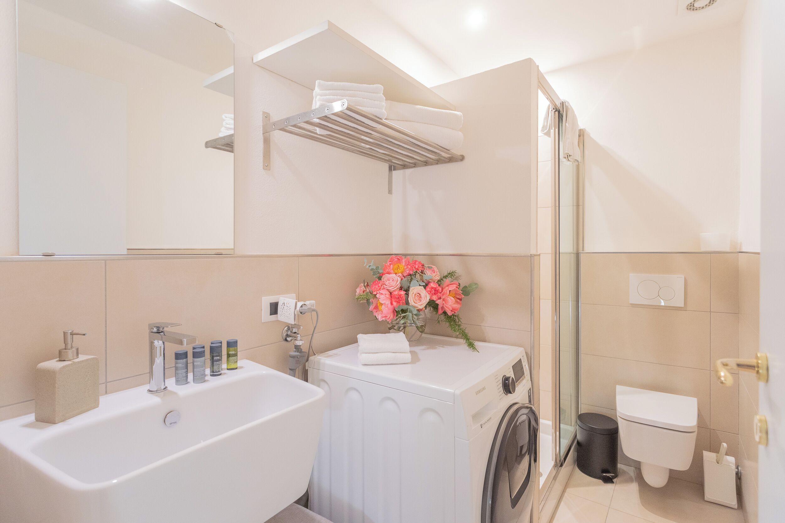 A modern bathroom with a bathtub, a washing machine, a toilet, and a glass shower enclosure.