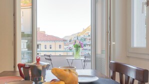 A dining area with a table set for two, a vase with flowers, and a view of buildings through a window. - White Lake View Apartment by Rent all Como (Como)