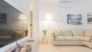 A modern living room with a flat-screen TV, a beige sofa, a floor lamp, and a small table with a vase of flowers. - White Lake View Apartment by Rent all Como (Como)
