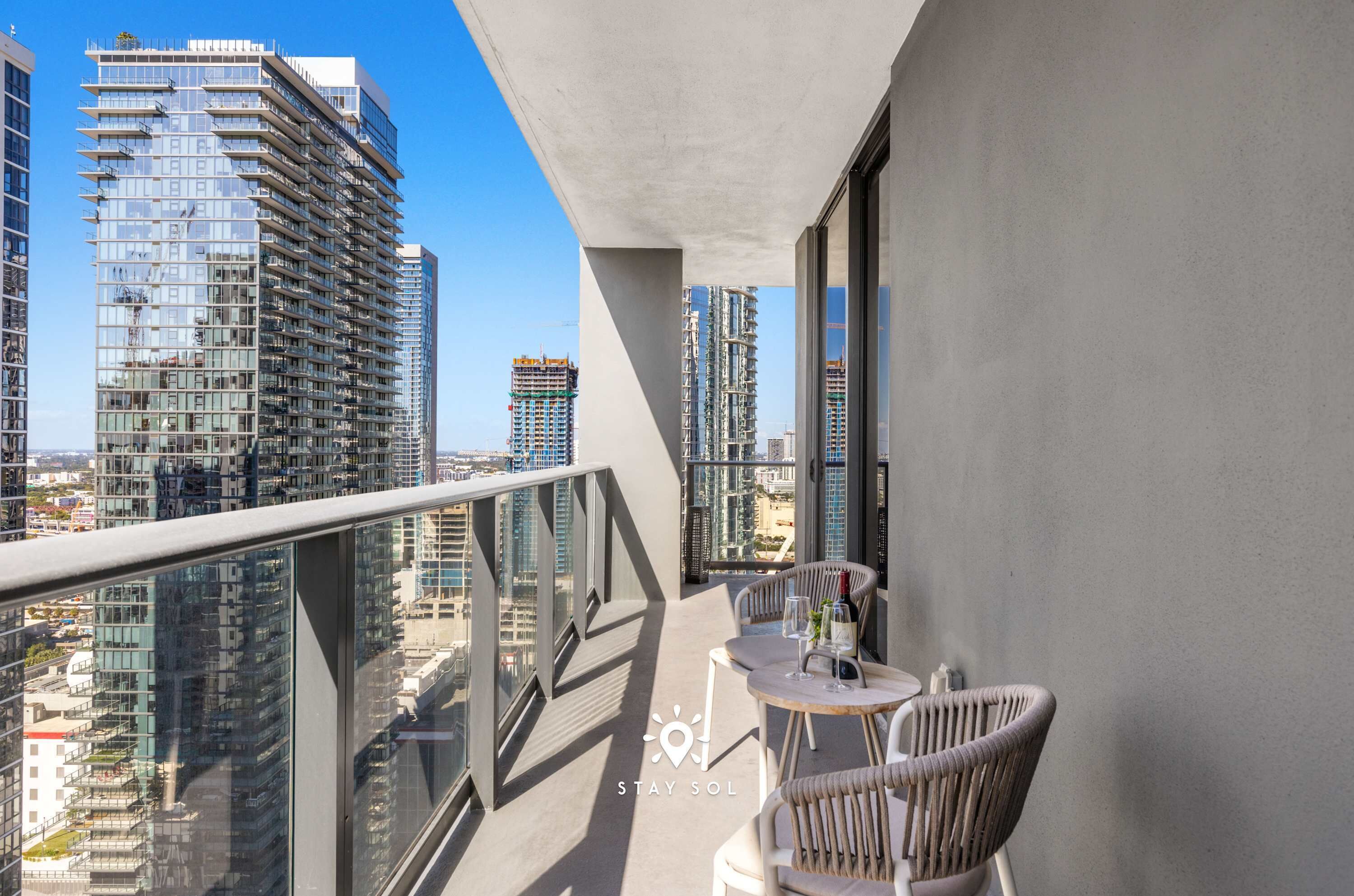 A balcony with a view of high-rise buildings, a table with chairs, and a glass of water.