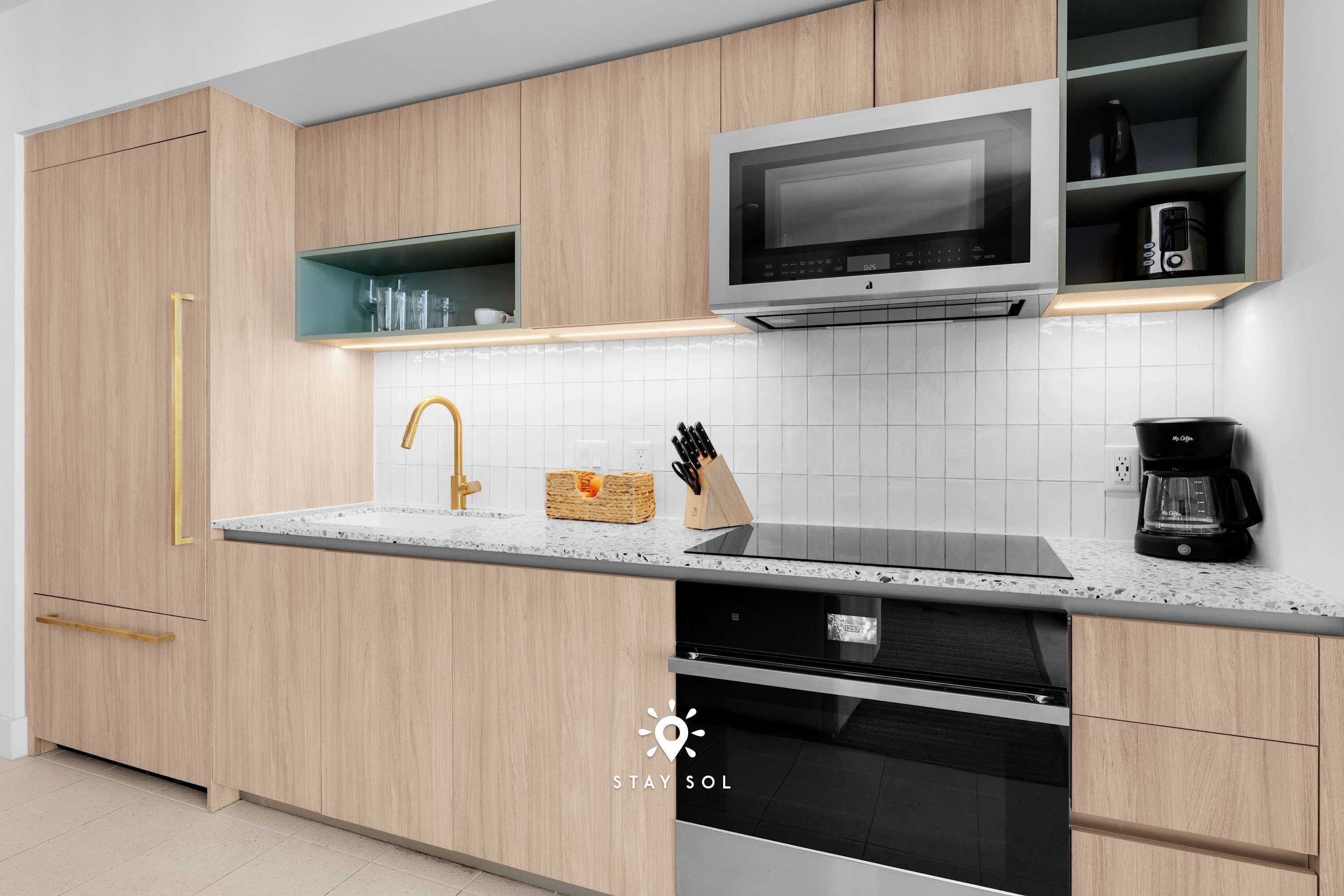 Une cuisine moderne avec des meubles en bois, un évier en acier inoxydable, un four à micro-ondes et une machine à café.