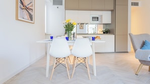 A modern kitchen with white cabinets, a microwave, and a dining area with two white chairs and a table. - Your Private Harbour Nearby George Clooney by Rent all Como (Carate Urio)