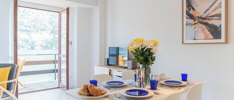Un moderno comedor con una mesa preparada para dos, un jarrón con flores amarillas y vistas al exterior a través de un ventanal.