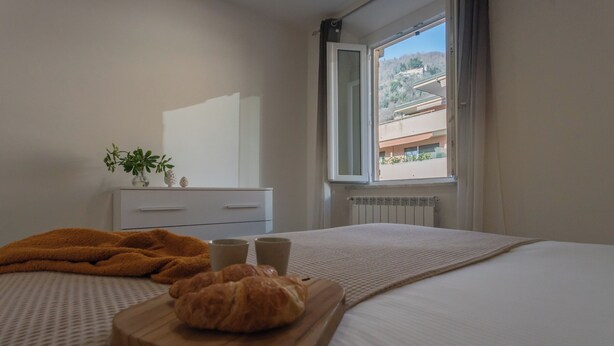 A bedroom with a bed, a wooden board with croissants, a small plant, and a window with a view of buildings. - Zezio 44 by Rent all Como (Como)
