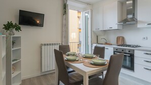 A modern kitchen with white cabinets, a gas stove, and a built-in oven. There is a dining table set with plates and glasses. - Zezio 44 by Rent all Como (Como)