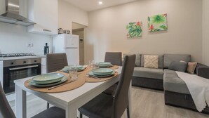 A modern kitchen with white cabinets, a gas stove, and a refrigerator. There is a dining table set with plates, glasses, and cutlery. A grey sofa and a coffee table are in the living area. - Zezio 44 by Rent all Como (Como)