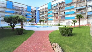 A multi-story residential building with balconies, a central courtyard with a pool, and well-maintained green lawns. - BLAUMARINA 225 Roses (Rosas / Roses)
