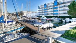 A marina with various boats docked, a building with balconies, and a clear sky. - BLAUMARINA 225 Roses (Rosas / Roses)