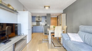 A modern living room with a grey sofa, a TV on a wooden stand, and a dining area with a table and chairs. - BLAUMARINA 225 Roses (Rosas / Roses)