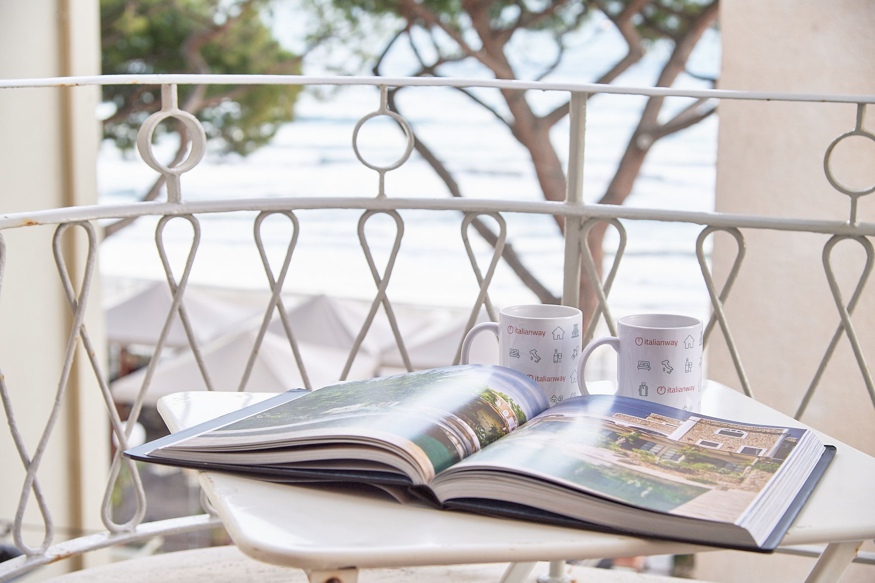 A metal balcony with a table holding a magazine and two coffee mugs.