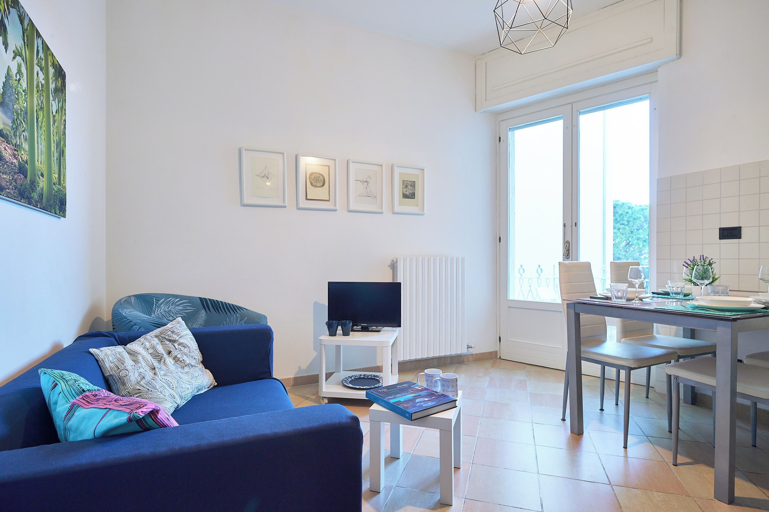 Ein modernes Wohnzimmer mit einem blauen Sofa, einem Couchtisch, einem Fernseher auf einem Schrank und einem Essbereich mit Tisch und Stühlen.