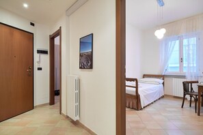 A bedroom with a bed, a chair, a radiator, a window with curtains, and a door. - Acquamarina in Alassio (Alassio)