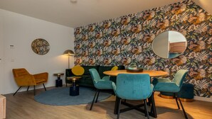 A modern living room with a floral wallpaper, a round dining table, and teal chairs. - Apartment in Zoutelande near the Beach (Zoutelande)