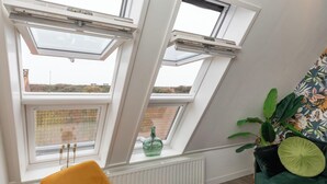 Ein Zimmer mit Dachfenstern, einem Heizkörper, einem gelben Stuhl und einer grünen Pflanze.