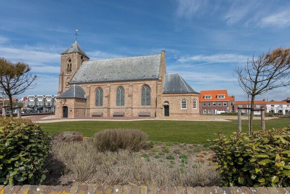 A historic church with a prominent tower and arched windows, surrounded by a well-maintained lawn and mature trees. - Romantic stay near Zoutelande (Zoutelande)