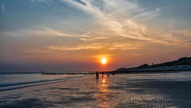 A sunset over a beach with a pier extending into the water. - Cozy Couple’s Escape (Zoutelande)