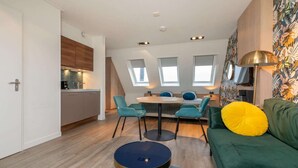 A compact living space with a kitchenette, a dining area, and a sofa with a yellow pillow. - Cozy Couple’s Escape (Zoutelande)