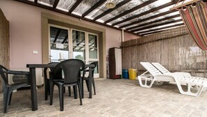 An outdoor patio with a table and chairs, a covered area with a ceiling, and a window with blinds. - Macine, one-bedroom terraced house (on two floors) (CECINA)