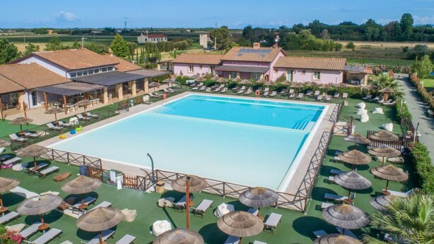A large swimming pool surrounded by sun loungers and umbrellas, with buildings in the background. - Macine, one-bedroom terraced house (on two floors) (CECINA)