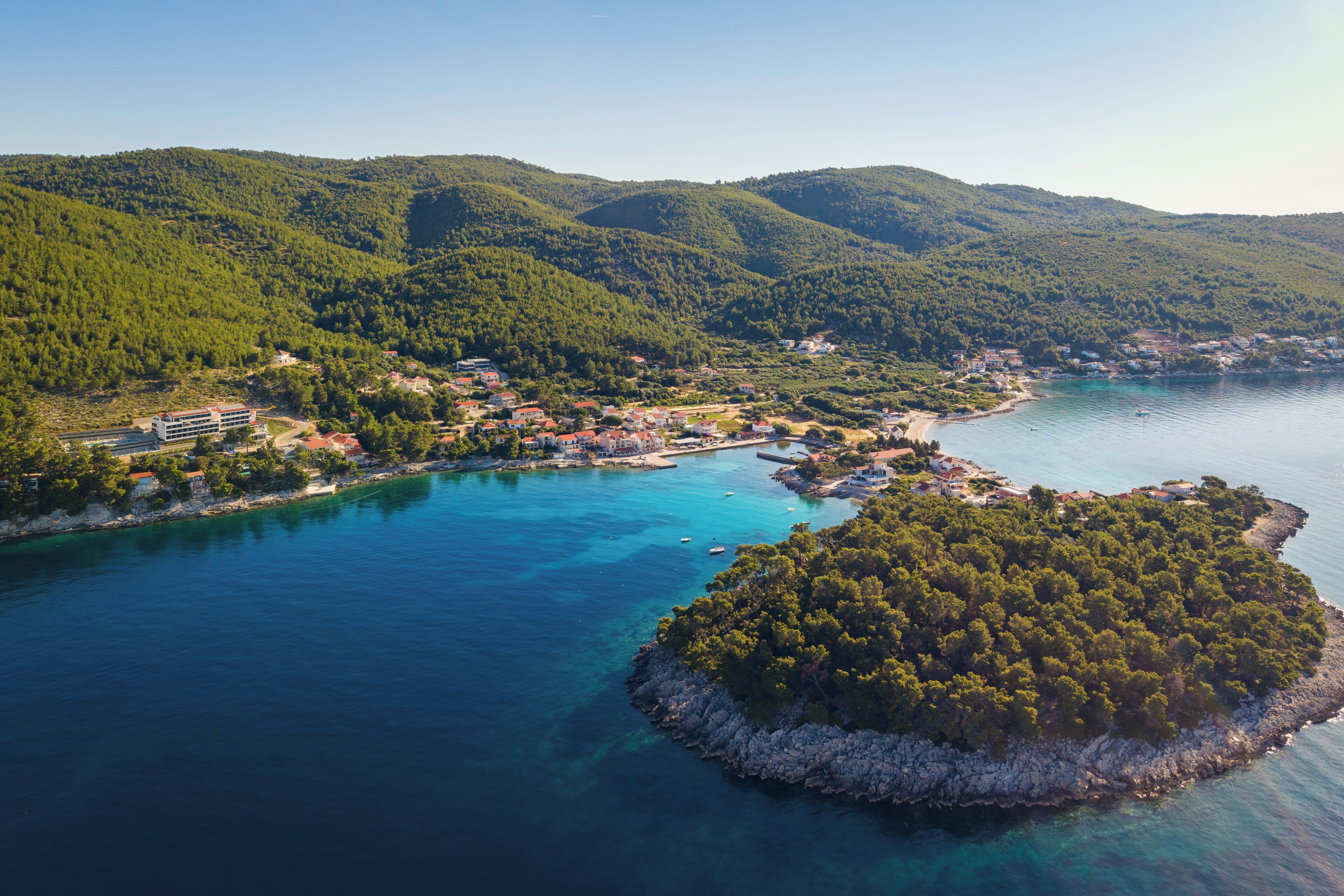 A coastal town with buildings along the shoreline, surrounded by hills and a small island.