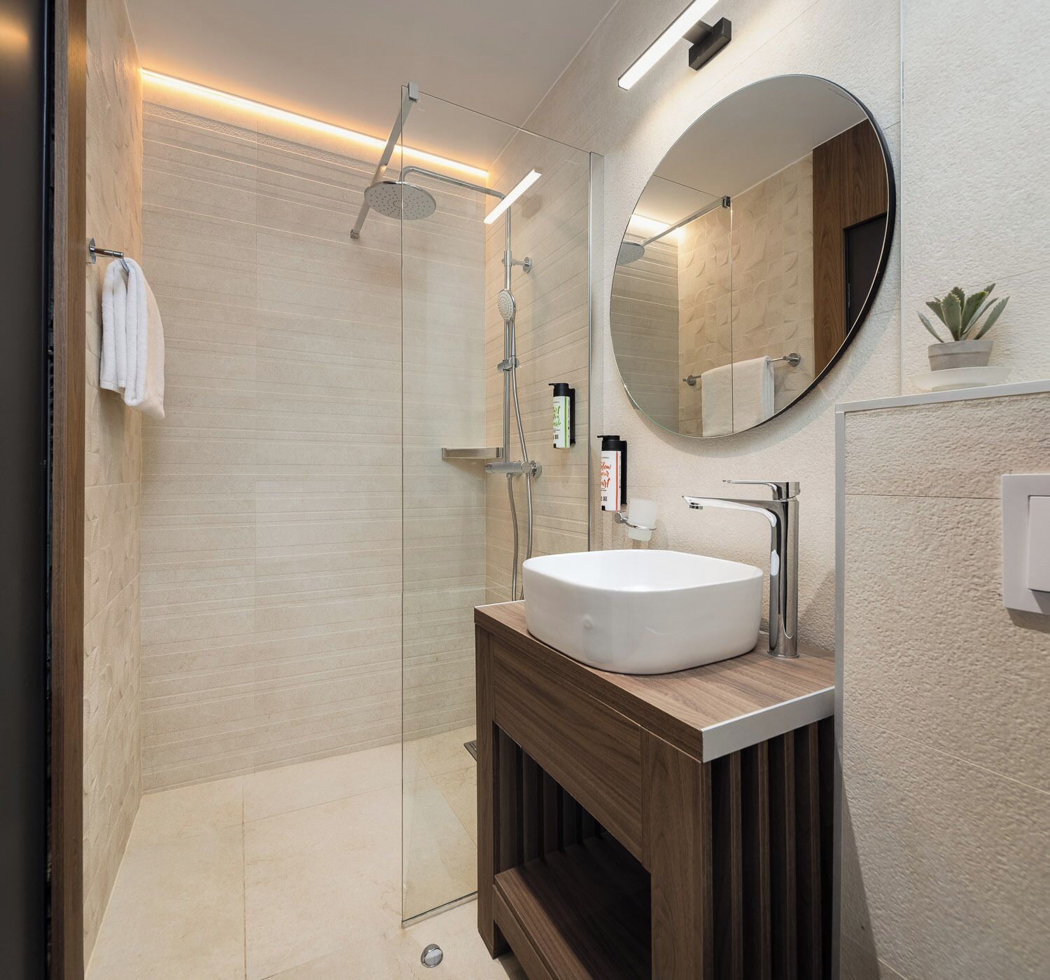 A modern bathroom with a glass-enclosed shower, a round mirror, and a wooden vanity with a white sink.