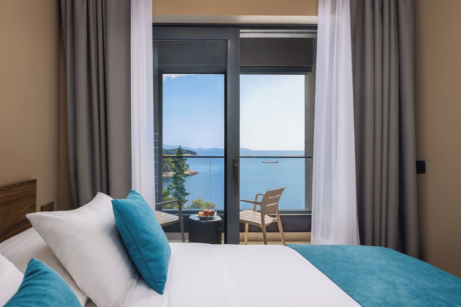 Habitación de hotel con cama, vista al mar y balcón con mesa y sillas.