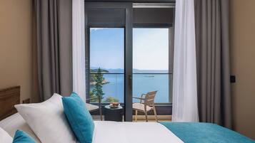 Habitación de hotel con cama, vista al mar y balcón con mesa y sillas.