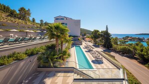 A resort with a swimming pool, lounge chairs, and a view of the sea. - Aminess Alfir Hotel (Blato)