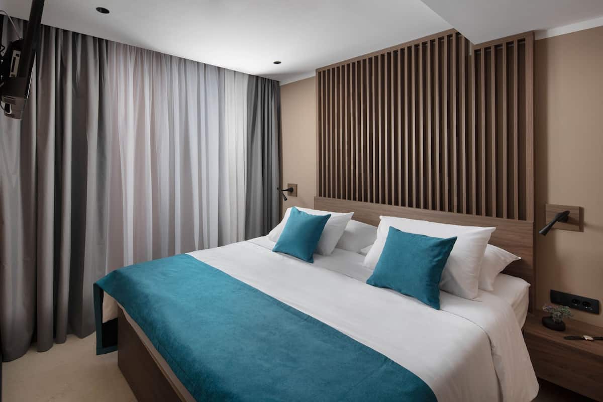 A modern hotel room with a large bed, a wooden headboard, a nightstand, and a wall-mounted lamp.
