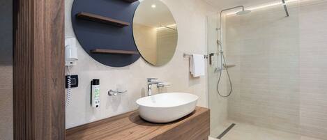 A modern bathroom with a round mirror, a wooden vanity, a white sink, and a glass shower enclosure.